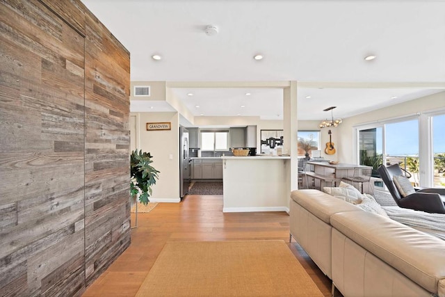 living room with recessed lighting, wood walls, visible vents, light wood-type flooring, and a chandelier