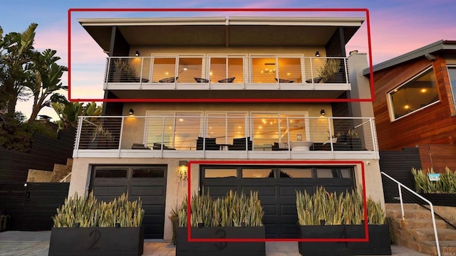 rear view of house featuring an attached garage, a balcony, and stucco siding