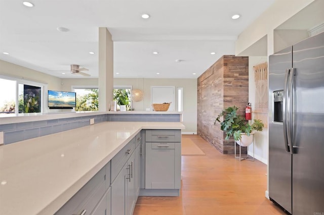kitchen with light wood-style floors, ceiling fan, gray cabinets, stainless steel refrigerator with ice dispenser, and light countertops