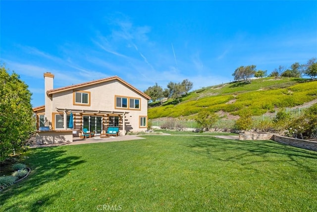 rear view of property with a chimney, a patio area, stucco siding, and a lawn