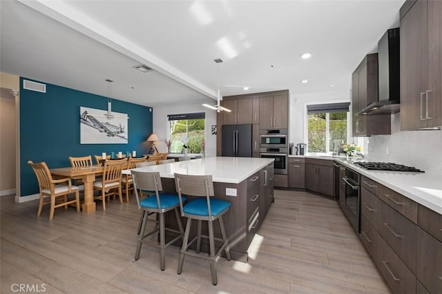 kitchen with wall chimney range hood, plenty of natural light, stainless steel appliances, and a kitchen bar