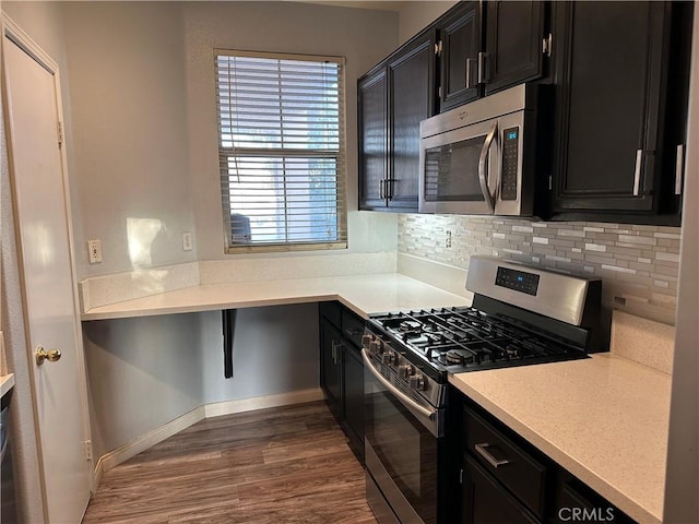 kitchen featuring light countertops, tasteful backsplash, dark cabinets, dark wood finished floors, and appliances with stainless steel finishes