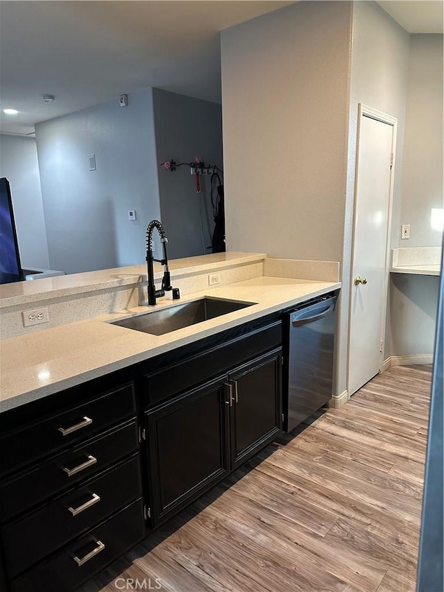 kitchen with a sink, dishwasher, dark cabinetry, light wood-style flooring, and baseboards