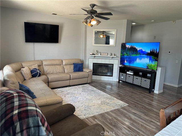living area featuring ceiling fan, a tiled fireplace, baseboards, wood finished floors, and visible vents
