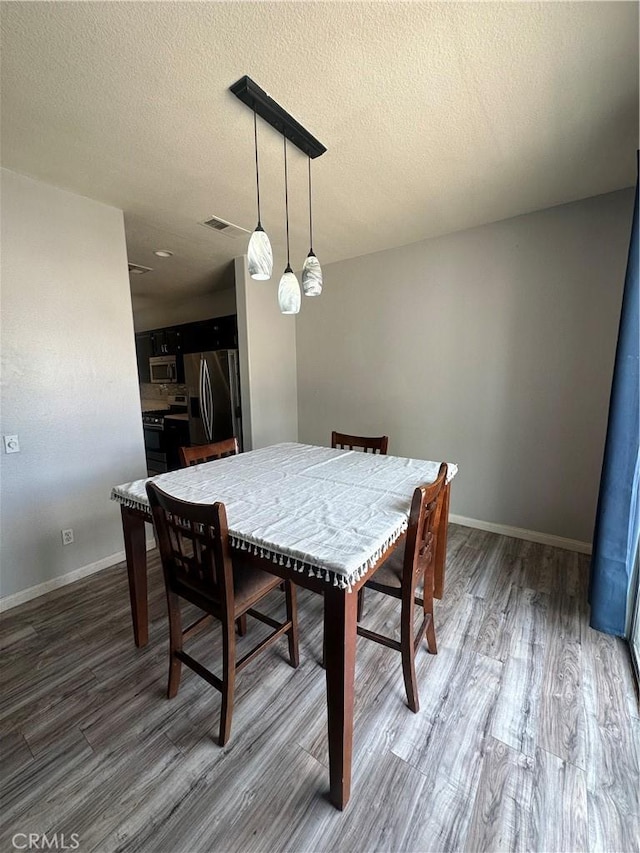 dining room featuring a textured ceiling, baseboards, and wood finished floors
