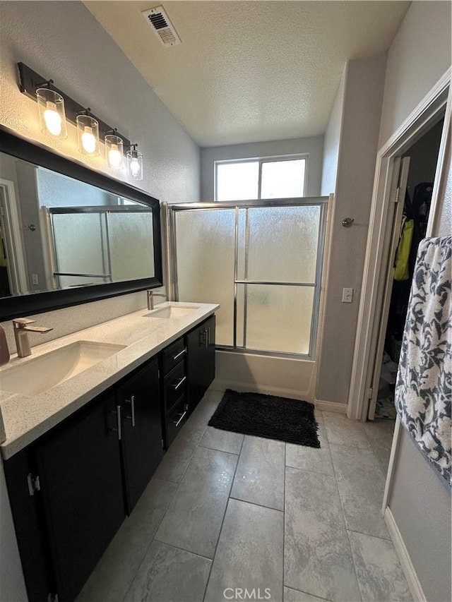 bathroom featuring a sink, shower / bath combination with glass door, double vanity, and visible vents