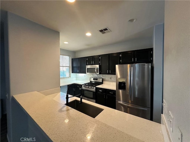 kitchen with visible vents, dark cabinets, a sink, appliances with stainless steel finishes, and backsplash