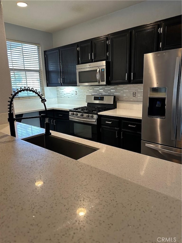 kitchen with dark cabinetry, stainless steel appliances, light stone countertops, and tasteful backsplash