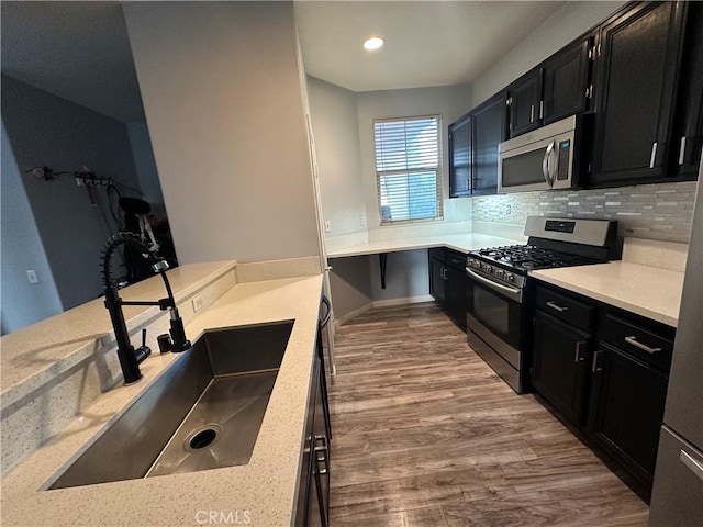 kitchen with appliances with stainless steel finishes, a sink, dark cabinetry, wood finished floors, and tasteful backsplash