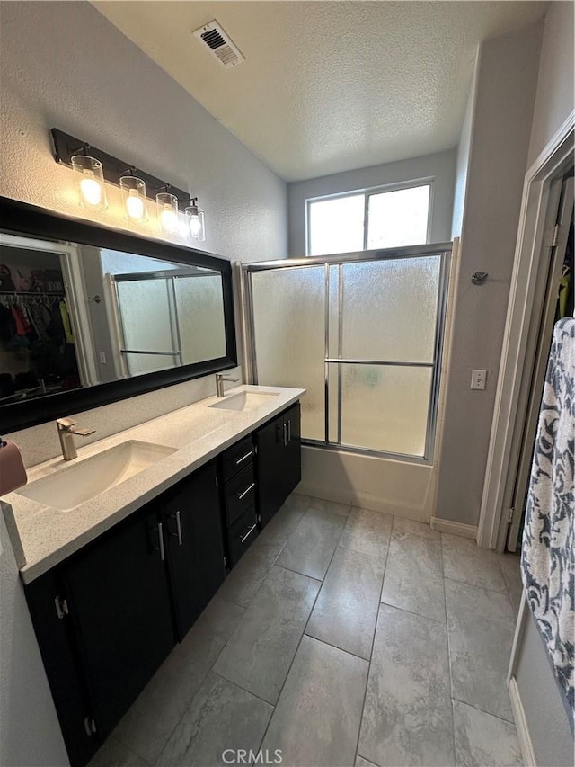 bathroom with double vanity, visible vents, combined bath / shower with glass door, and a sink