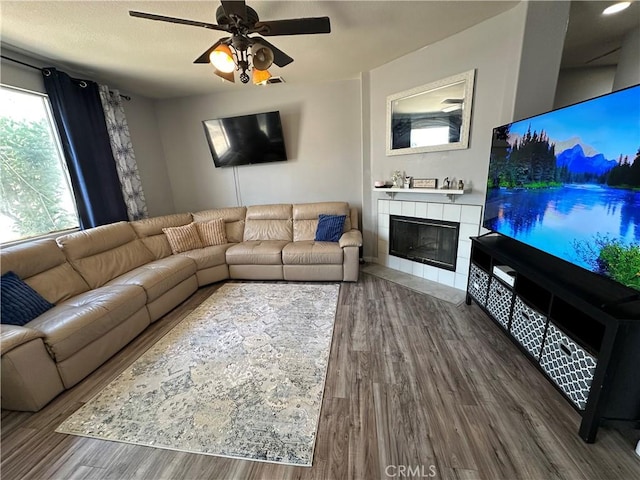 living area with visible vents, ceiling fan, wood finished floors, and a tile fireplace