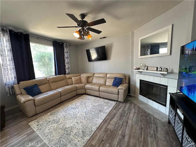 living area featuring a ceiling fan, visible vents, wood finished floors, a tile fireplace, and baseboards
