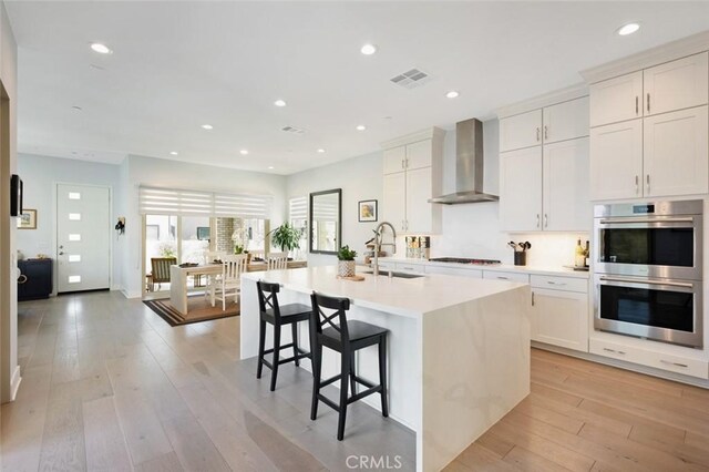 135 Bosal, Irvine, CA 92618 - kitchen with wall chimney exhaust hood, a sink, double oven, a center island with sink, and light countertops