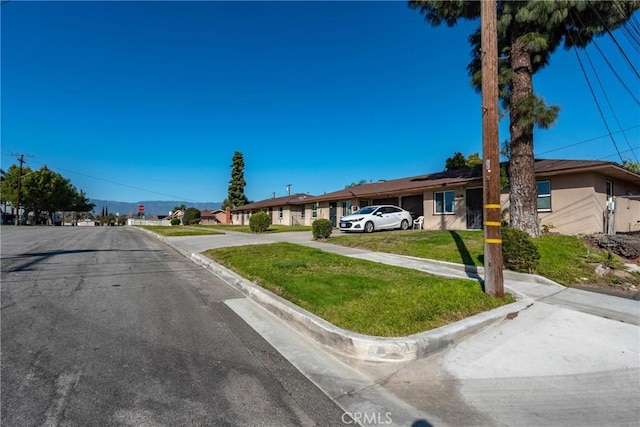 view of front facade featuring stucco siding, roof mounted solar panels, a residential view, and a front lawn