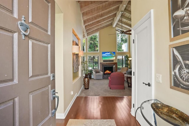 foyer entrance with beam ceiling, high vaulted ceiling, a warm lit fireplace, wood-type flooring, and ceiling fan