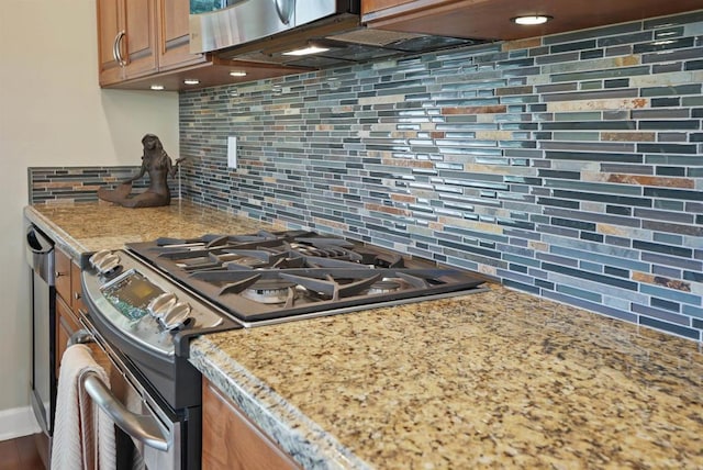 kitchen featuring gas range, light stone countertops, brown cabinetry, and backsplash