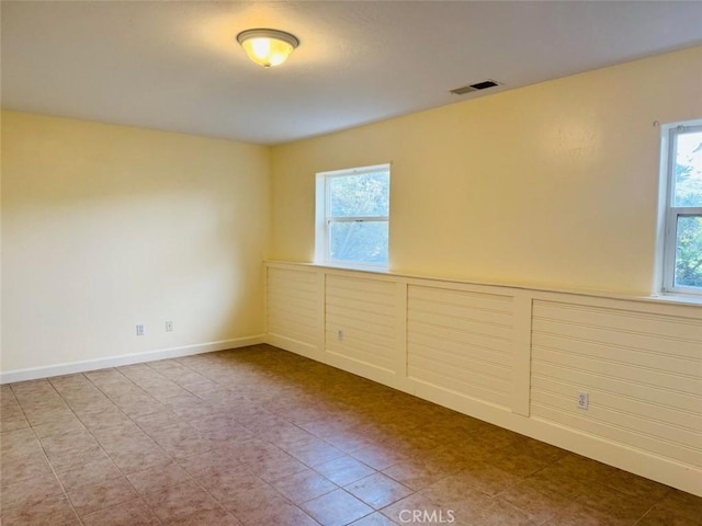 empty room featuring a wealth of natural light, visible vents, baseboards, and wainscoting