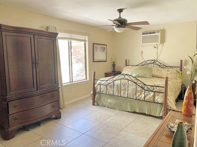 bedroom with a wall unit AC, light tile patterned flooring, baseboards, and ceiling fan