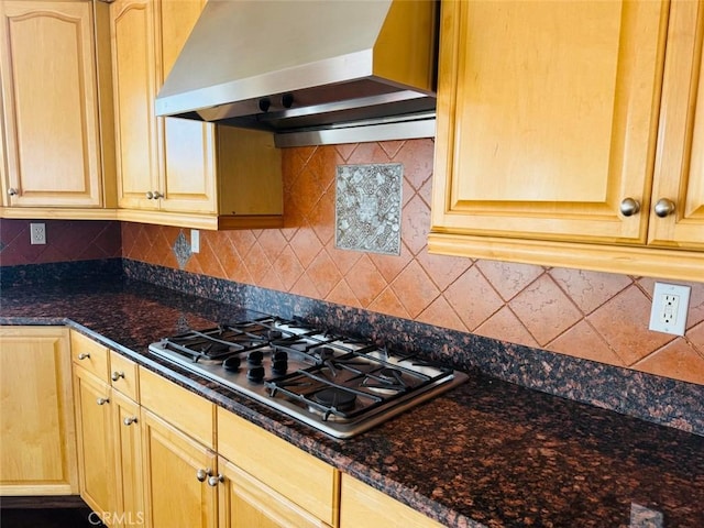 kitchen with decorative backsplash, dark stone countertops, wall chimney range hood, and stainless steel gas cooktop