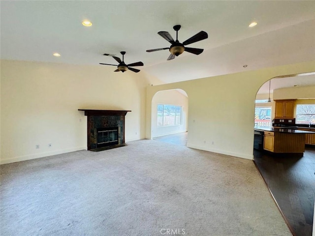 unfurnished living room featuring baseboards, a tiled fireplace, recessed lighting, arched walkways, and a ceiling fan