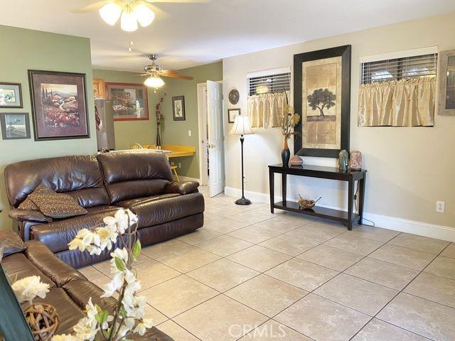 living area featuring light tile patterned floors, a ceiling fan, and baseboards