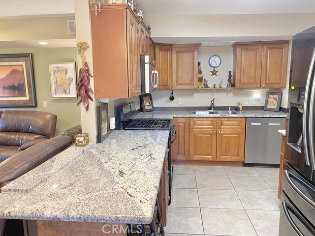 kitchen featuring visible vents, light tile patterned flooring, a sink, stainless steel appliances, and brown cabinets