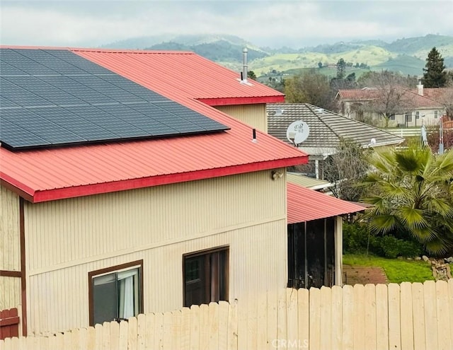 view of property exterior featuring roof mounted solar panels, a mountain view, metal roof, and fence