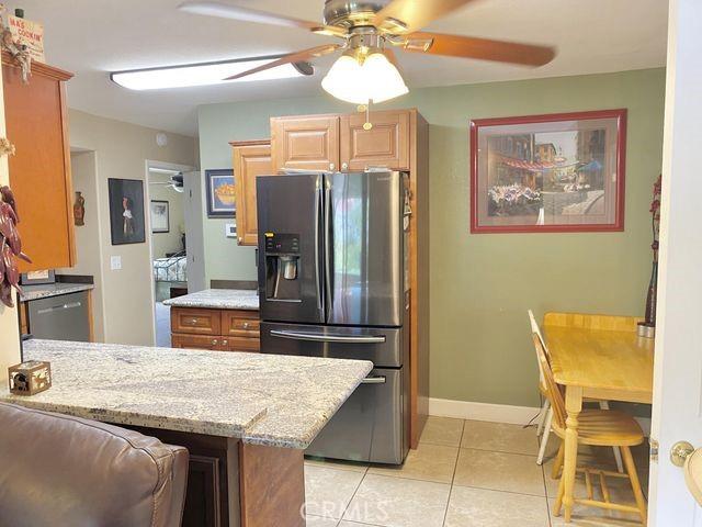 kitchen with light stone counters, a ceiling fan, light tile patterned flooring, dishwasher, and refrigerator with ice dispenser