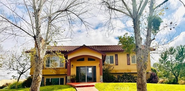 rear view of property featuring a tile roof, a lawn, and stucco siding