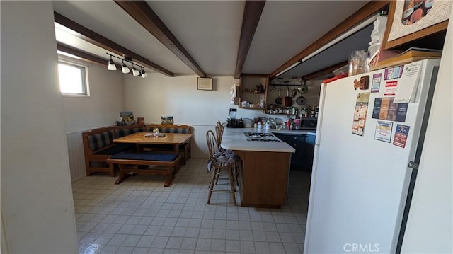 kitchen with light countertops, a kitchen bar, stainless steel gas cooktop, beamed ceiling, and freestanding refrigerator