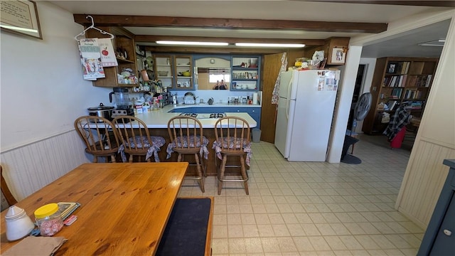 kitchen with wainscoting, open shelves, beam ceiling, and freestanding refrigerator