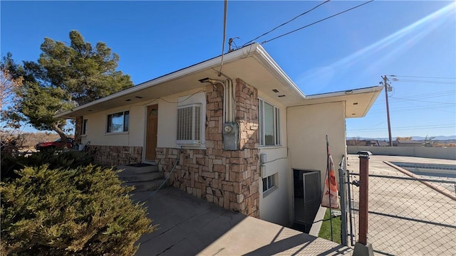 view of side of property featuring stone siding, stucco siding, and fence