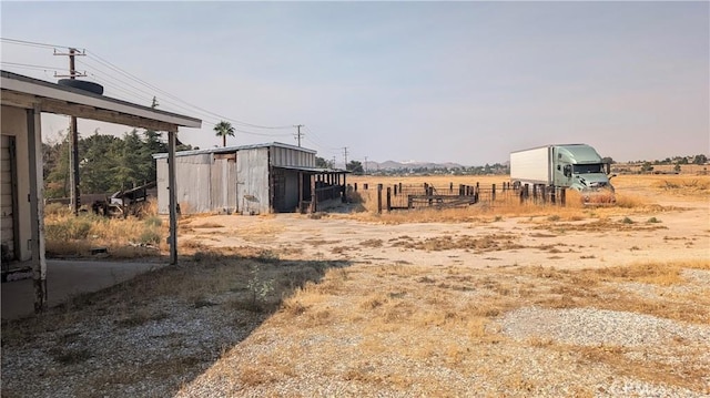 view of yard featuring a rural view, fence, a pole building, and an outdoor structure