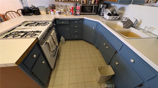 kitchen featuring light countertops, range with gas stovetop, stainless steel microwave, a sink, and blue cabinets