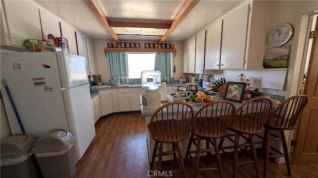 kitchen featuring dark wood-style flooring, white cabinets, a peninsula, beam ceiling, and freestanding refrigerator
