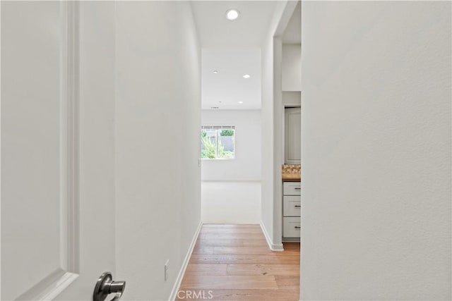 hallway with light wood finished floors, arched walkways, baseboards, and recessed lighting