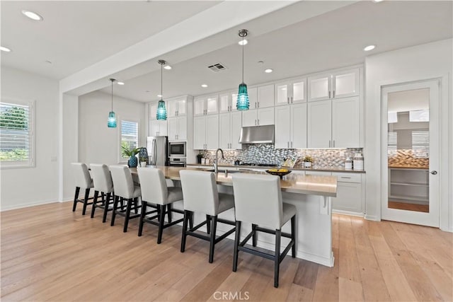 kitchen featuring under cabinet range hood, plenty of natural light, visible vents, backsplash, and appliances with stainless steel finishes