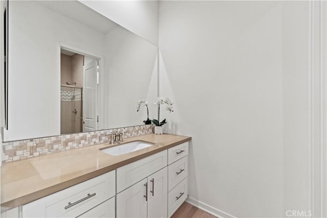 bathroom with a shower with door, baseboards, vanity, wood finished floors, and tasteful backsplash