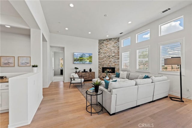 living area with light wood-type flooring, visible vents, a stone fireplace, and recessed lighting