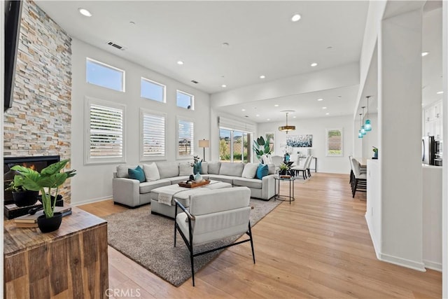 living area with a stone fireplace, light wood-type flooring, visible vents, and recessed lighting