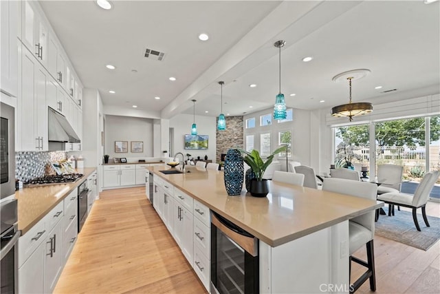 kitchen featuring wine cooler, plenty of natural light, under cabinet range hood, white cabinets, and tasteful backsplash