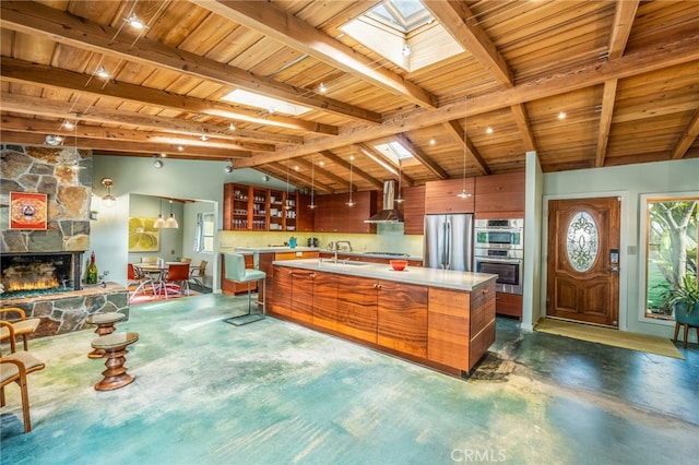 kitchen with a sink, light countertops, appliances with stainless steel finishes, wall chimney range hood, and brown cabinets