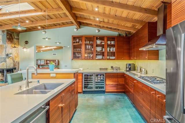 kitchen with a sink, wine cooler, appliances with stainless steel finishes, brown cabinetry, and wall chimney range hood