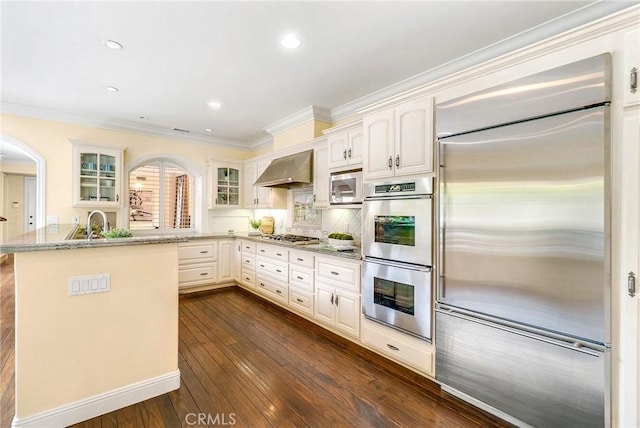 129 Via Waziers, Newport Beach, CA 92663 - kitchen with appliances with stainless steel finishes, wall chimney exhaust hood, glass insert cabinets, ornamental molding, and dark wood-style flooring