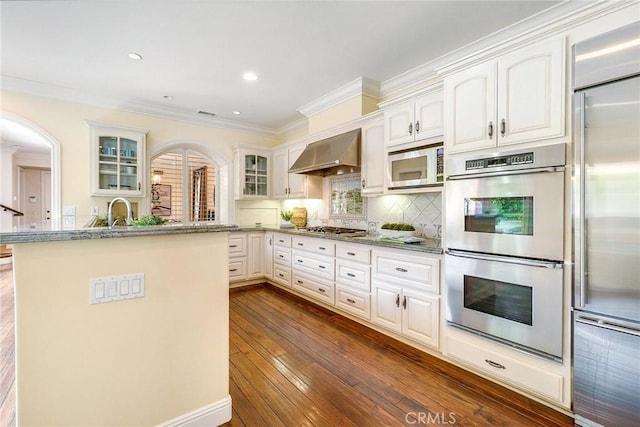129 Via Waziers, Newport Beach, CA 92663 - kitchen with built in appliances, wall chimney exhaust hood, crown molding, arched walkways, and glass insert cabinets