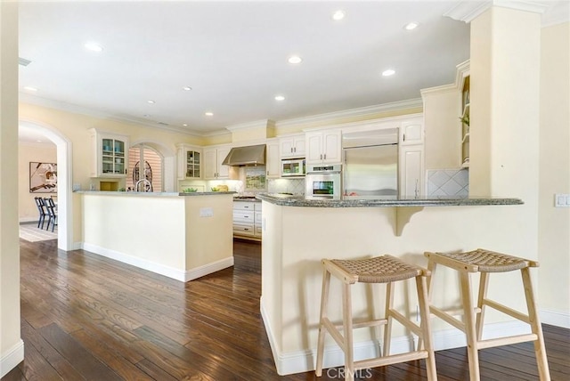 129 Via Waziers, Newport Beach, CA 92663 - kitchen with a peninsula, wall chimney exhaust hood, appliances with stainless steel finishes, arched walkways, and glass insert cabinets