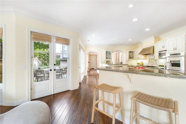 129 Via Waziers, Newport Beach, CA 92663 - kitchen featuring appliances with stainless steel finishes, glass insert cabinets, a kitchen bar, dark stone countertops, and french doors