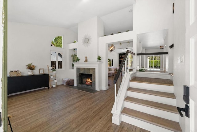 stairway with baseboards, a fireplace, wood finished floors, and high vaulted ceiling