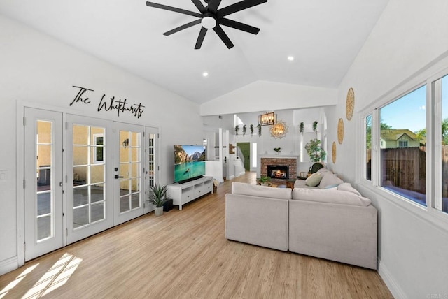 living area featuring a fireplace, french doors, ceiling fan with notable chandelier, wood finished floors, and vaulted ceiling