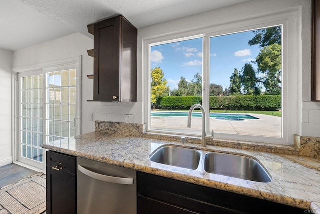 kitchen with dark brown cabinets, light stone countertops, a sink, dishwasher, and tasteful backsplash